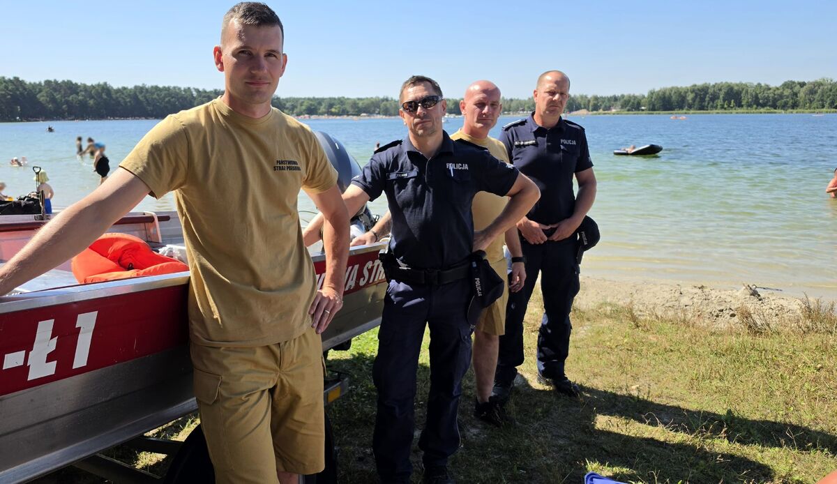 policjanci i strażacy przy łodzi na plaży, w tle widać jezioro