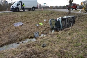 W przydrożnym rowie lezący na boku osobowy citroen, na jezdni uszkodzony bus obok policjant