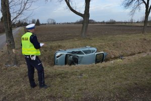 W przydrożnym rowie wywrócony samochód obok policjant wypełnia protokoły