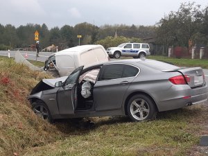 Pojazd marki BMW w przydrożnym rowie z rozbitym przodem. W dalszym planie w rowie citroen oraz na poboczu policyjny radiowóz