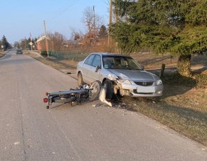 Leżący na jezdni uszkodzony motocykl marki MZ. Po prawej stronie na poboczu jezdni pojazd marki Mazda z uszkodzonym przodem