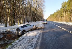 Pojazd marki Volkswagen Golf w przydrożnym rowie. Po prawej na jezdni zaparkowany oznakowany radiowóz policji.