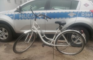 Odzyskany przez policjantów rower zabezpieczony na policyjnym parkingu. W tle oznakowany policyjny radiowóz.