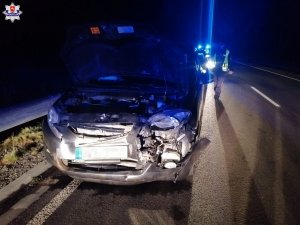 pora nocna, uszkodzony przód pojazdu marki Honda, w tle idący w jego kierunku policjant