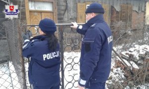 dwóch umundurowanych policjantów przy bramie posesji