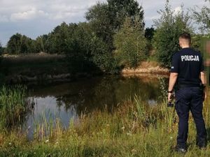 policjant stojący z mężczyzną, który pokazuje mu sadzawkę - zbiornik wodny do którego wpadł 3latni chłopiec