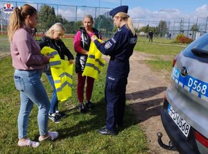 na zdjęciu widoczna jest policjantka ktora rozdaje kamizelki odblaskowe uczestnikom festynu