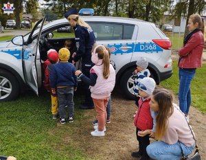 na zdjęciu widoczne są dzieci z rodzicami ,stojący  radiowóz i policjantka