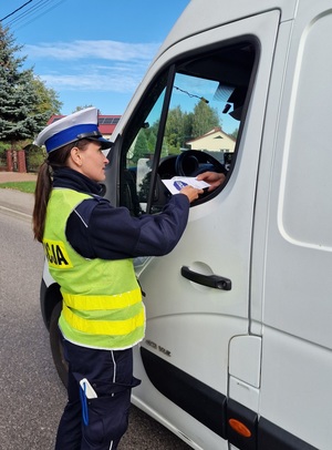 policjantka w kamizelce odblaskowej wręczająca kierowcy ulotkę