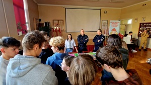 policjanci i przedstawiciel PCPR rozdający ulotki profilaktyczne uczniom