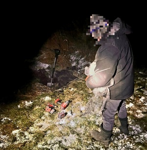 mężczyzna wykopujący nocą skradzione przedmioty zakopane na polu