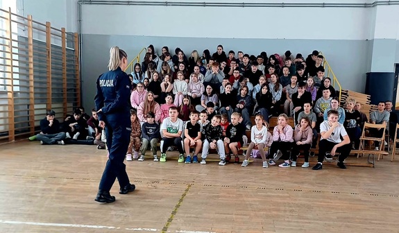 policjanta przed grupą uczniów siedzącą na trybunach