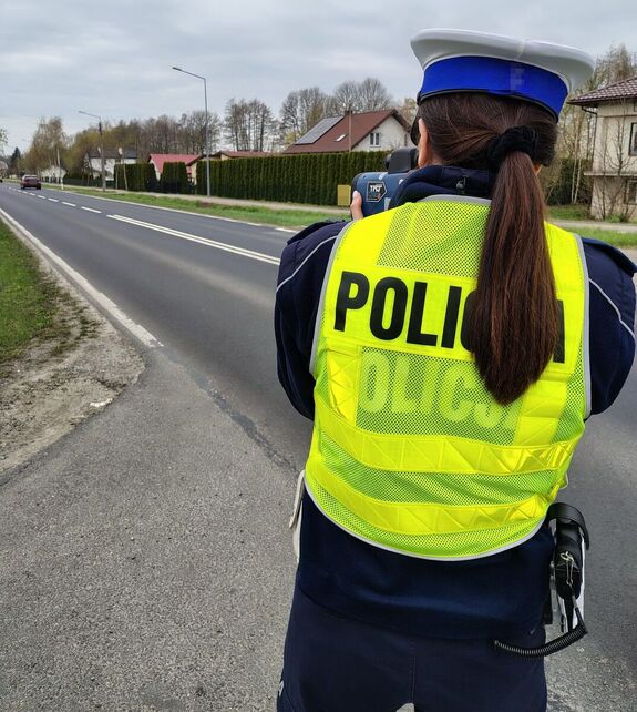 ;policjantka tyłem wykonująca pomiar ręcznym miernikiem prędkości