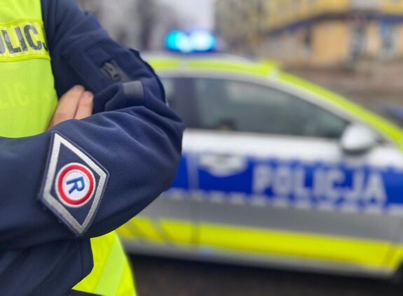 ramię umundurowanego policjanta na tle radiowozu