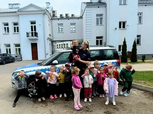 policjantka z grupą przedszkolaków przy oznakowanym radiowozie