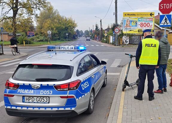 policjant, oznakowany radiowóz oraz osoba poruszająca się hulajnogą